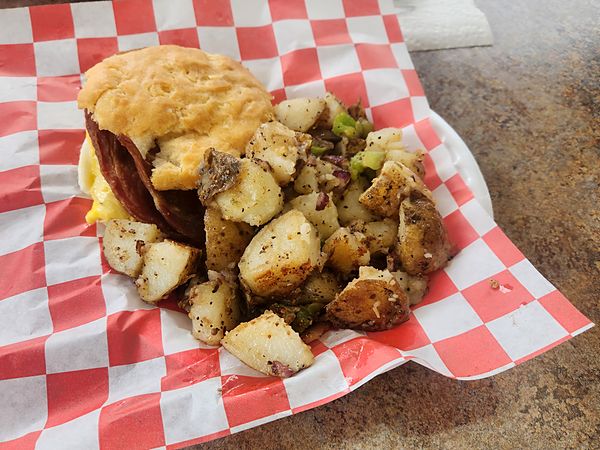 Breakfast biscuit with seasoned home fries in a red-checkered basket