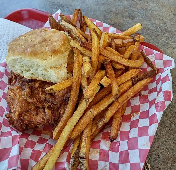 Fried chicken with a biscuit and seasoned fries in a red-checkered basket