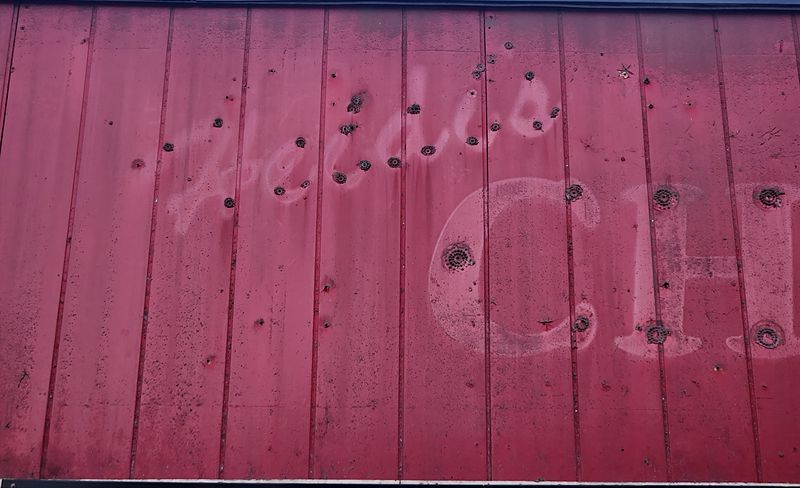 Faded script Heidi’s and large CH letters ghosted on the red vertical siding, ringed by the bolt holes where the old sign letters hung