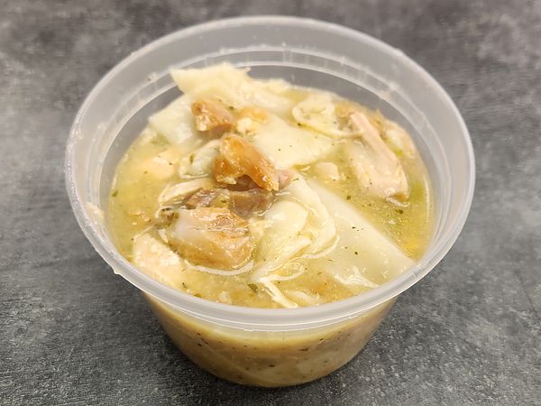 A clear deli cup of chicken and dumplings in broth, with shredded chicken and flat dumplings