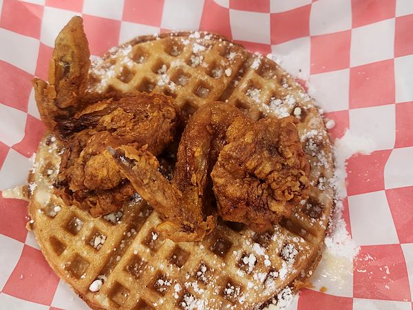 Fried chicken wings on a powdered-sugar waffle, on red-checkered paper
